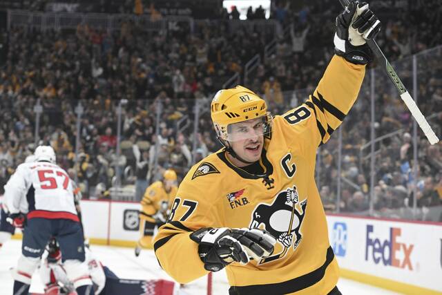Sidney Crosby of the Pittsburgh Penguins raising his stick after scoring a goal, wearing the 2025/26 Gold third jersey