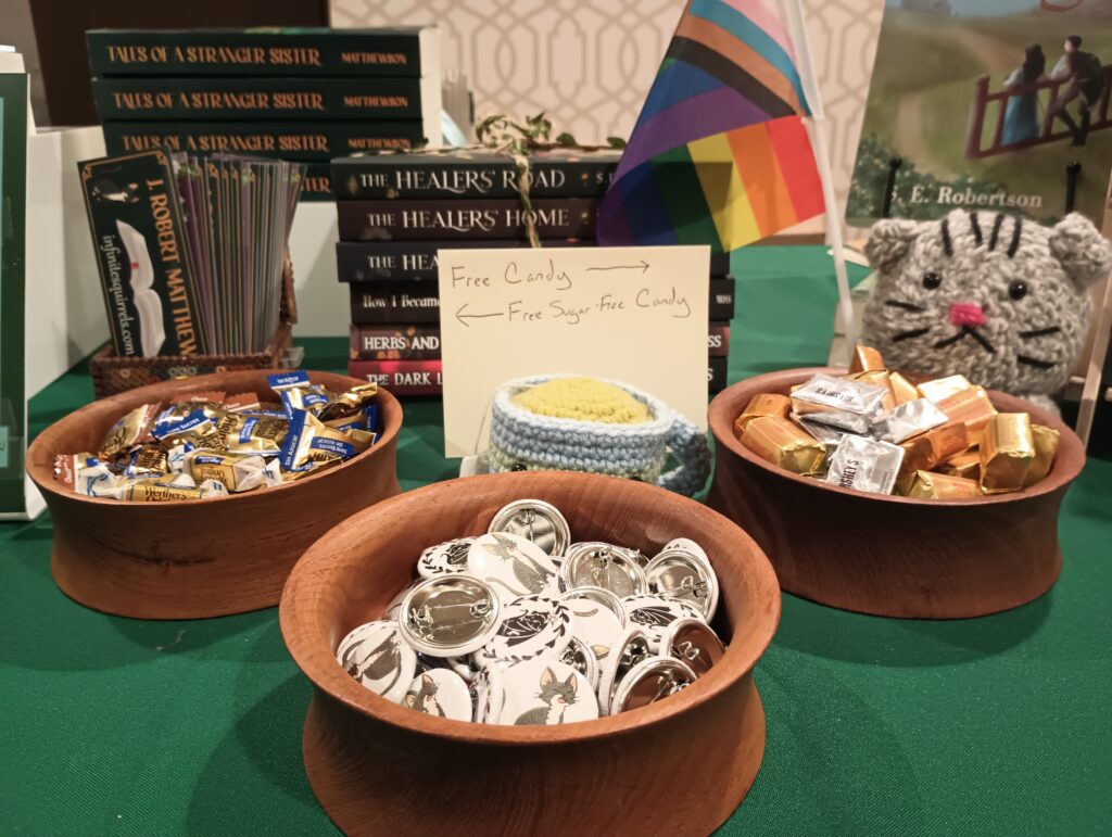 Wooden bowls filled with Candy and Pins, next to a sign indication which is sugared and which is sugar-free. A plush cat doll holds a pride flag.