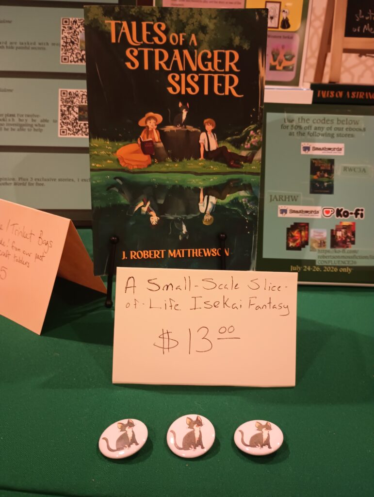 A paperback copy of "Tales of a Stranger Sister" with a price sign.  In front of the sign are three pins featuring Rose the Kitten from the book. 